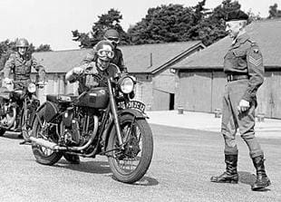 Trainee Dispatch Rider undfer the beady eye of instructor pushes his Matchless G3L classic motorcycle during the Second World War
