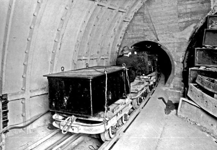 From the archives: Wearing just a trilby as head protection, a Post Office Underground Railway worker enters a tunnel during the line’s operational days with a ‘freight train’ carrying a transformer secured by rope on a flat truck. THE POSTAL MUSEUM 