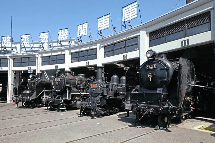 Four locos outside the historic Umekoji roundhouse. From right to left: powerful 4-6-4 C62 1, built by Hitachi in 1948, and 4-4-2T Number 1080, built in Scotland by Dubs in 1901 as a 4-4-0 tender loco (rebuilt in 1926 to the current 4-4-2T design). Nearer the camera are two Kawasaki-built locos, 2-8-0 9633 (right), dating from 1914, and (left) 1935 vintage 2-6-4T C11 64. Between 1932 and 1947, 381 C11s were built. Fifty have been preserved, including five that are currently in working order. JAMES WAITE